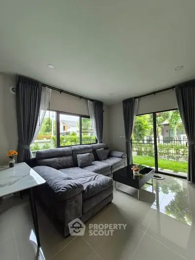 Spacious living room with large windows and garden view, featuring a modern gray sectional sofa and elegant decor.