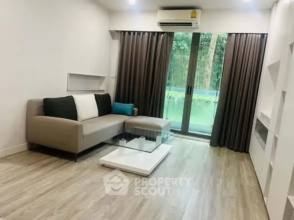 Modern living room with sleek sofa, glass coffee table, and large window offering serene garden view.