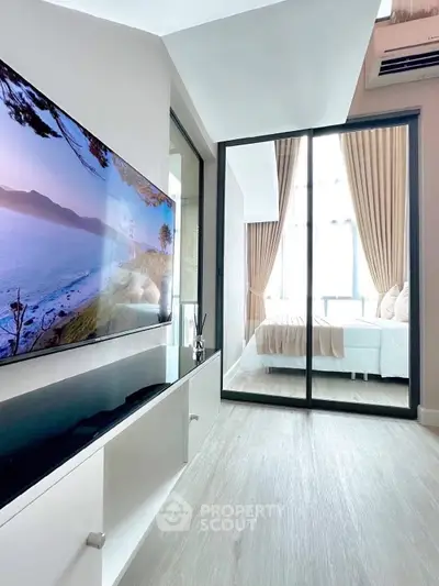 Modern apartment interior with sleek TV setup and glass sliding doors leading to a bright bedroom.