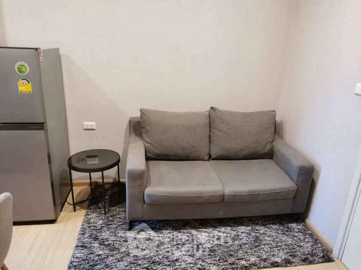 Cozy living room with gray sofa and modern fridge in a compact apartment.