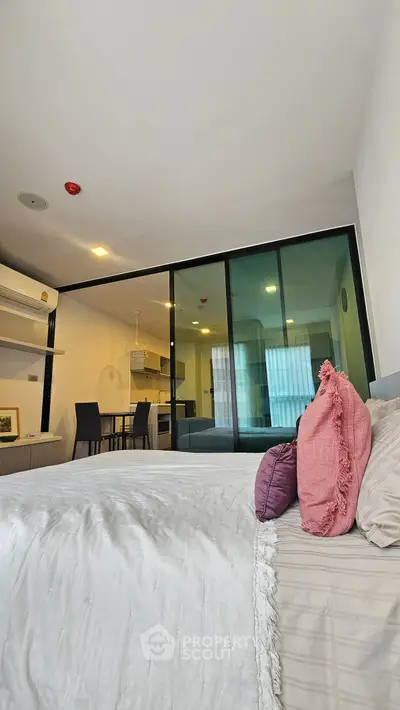 Modern bedroom with glass partition and view into stylish kitchen area.