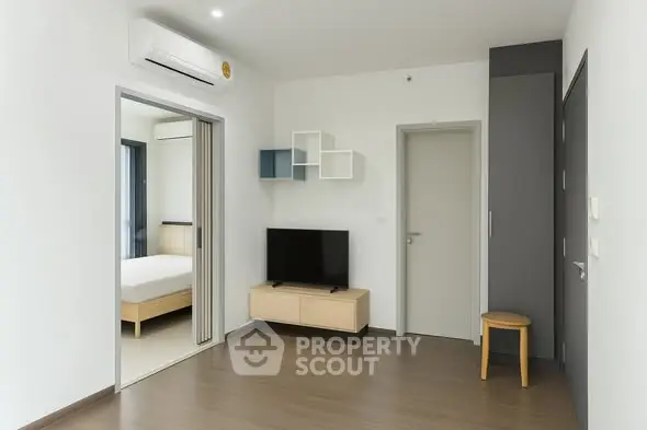 Modern minimalist living room with TV and air conditioning, featuring a view into a cozy bedroom.