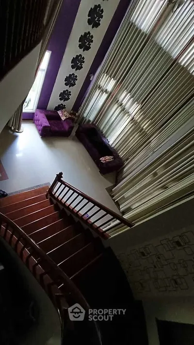 Elegant living room with high ceilings, stylish purple accents, and a wooden staircase, perfect for modern living.