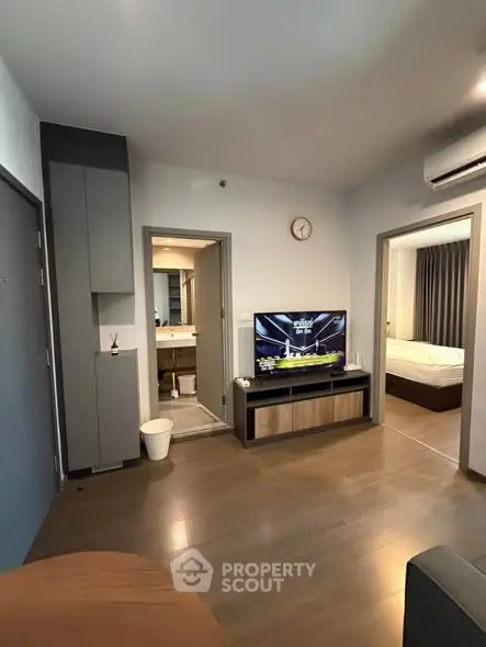 Modern apartment interior with open living space and visible bedroom, featuring sleek design and wooden flooring.