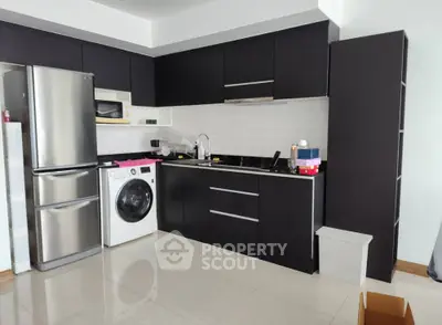 Modern kitchen with sleek black cabinets and integrated appliances including washing machine and fridge.