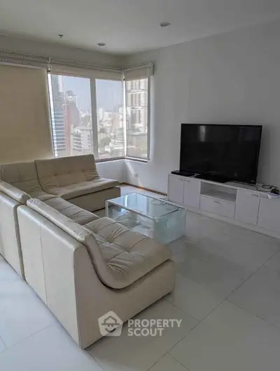 Spacious modern living room with city view, featuring sleek white sofas and a large flat-screen TV.