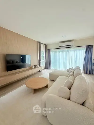 Spacious modern living room with large sofa and wall-mounted TV, featuring floor-to-ceiling windows.