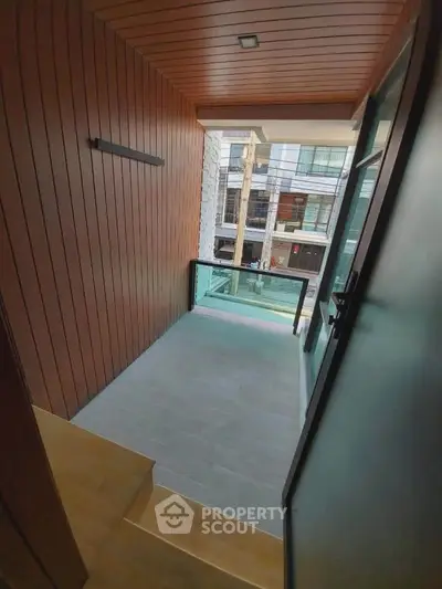 Modern balcony with wooden paneling and glass railing overlooking urban street view.