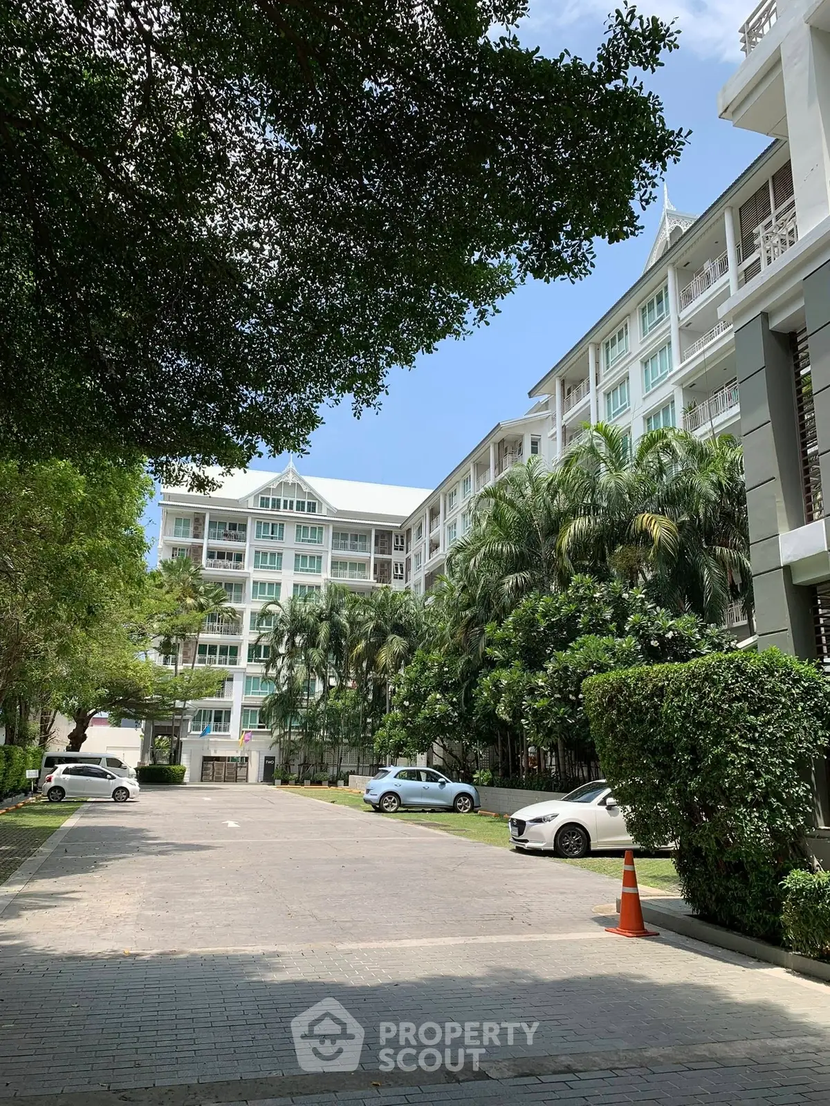 Elegant residential building with lush greenery and spacious parking area.