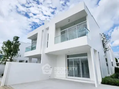 Modern white two-story house with large windows and balcony under a blue sky.