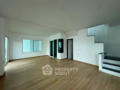 Spacious modern living room with wooden flooring and staircase in a bright open layout.