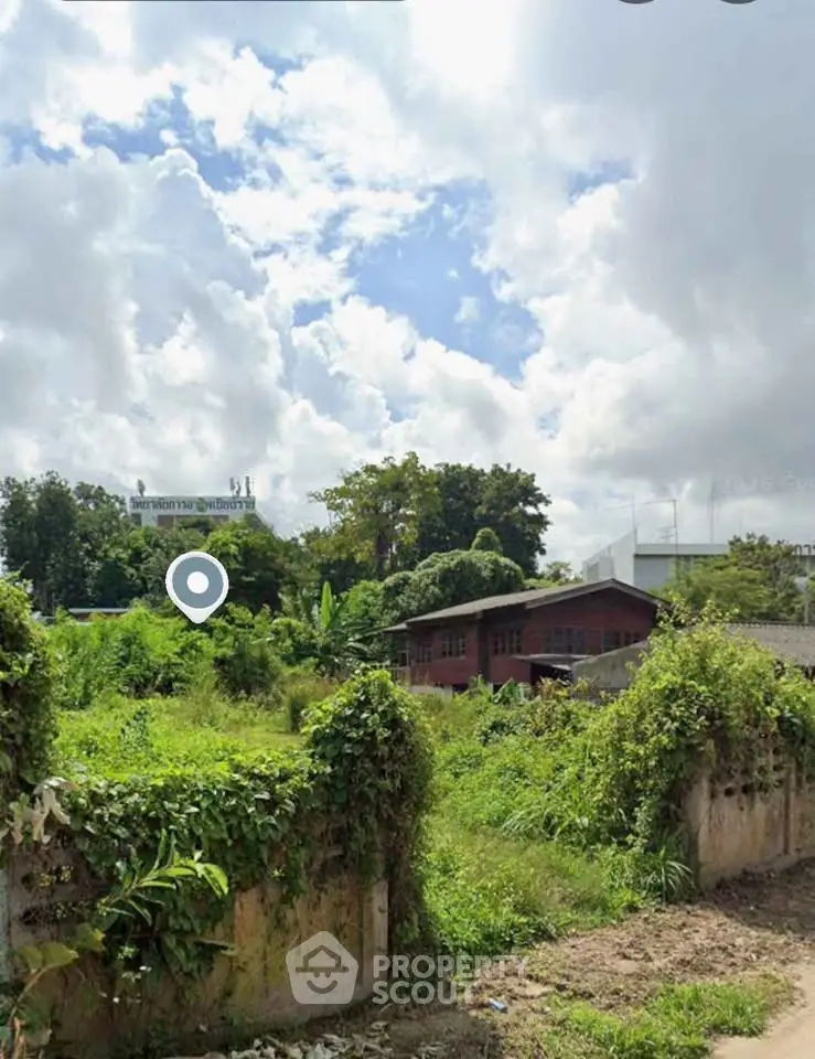 Scenic view of lush green land with rustic buildings under a cloudy sky, ideal for development.