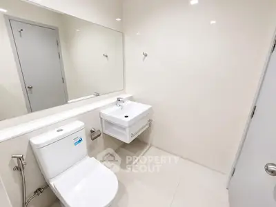 Modern bathroom with sleek fixtures and minimalist design, featuring a wall-mounted sink and large mirror.