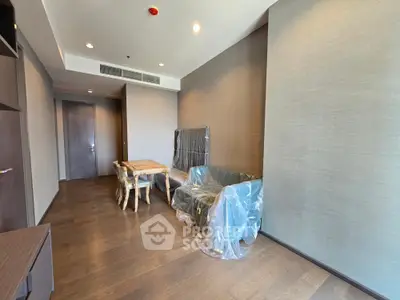 Modern living room with wooden flooring and furniture covered in protective plastic, ready for move-in.