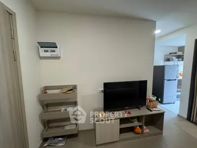 Modern living room with TV and open kitchen featuring a sleek refrigerator.