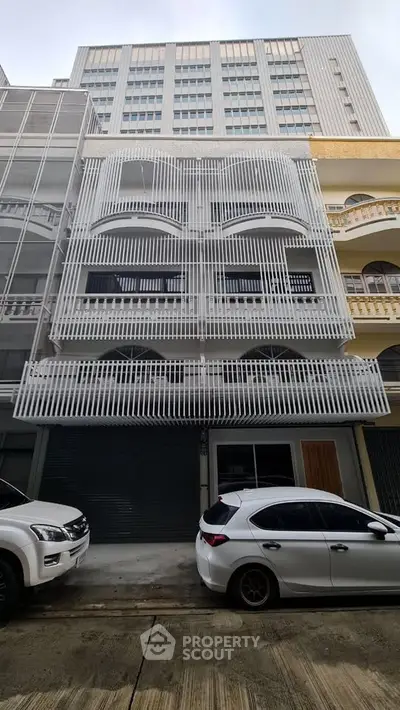 Modern multi-story building with unique facade design and street parking in urban setting.
