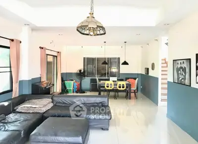 Spacious living room with modern decor and natural light, featuring a cozy black leather sofa and stylish pendant lighting.
