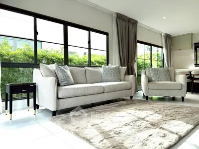 Spacious living room with modern sofa set and large windows offering lush garden views.