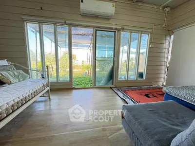 Bright living room with large windows and garden view, featuring cozy seating and air conditioning.