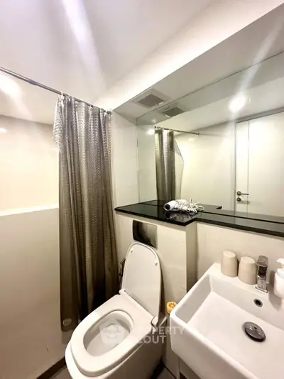 Modern bathroom with sleek fixtures and large mirror, featuring a toilet and sink.