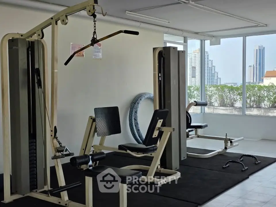 Spacious gym with modern equipment and city view, perfect for fitness enthusiasts.