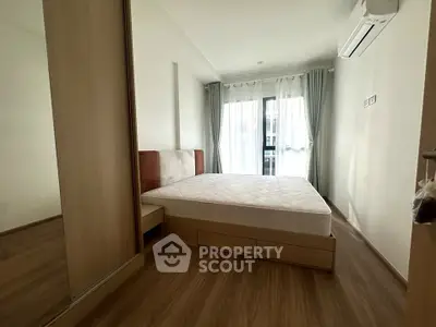 Modern bedroom with large window and wooden flooring in a stylish apartment.