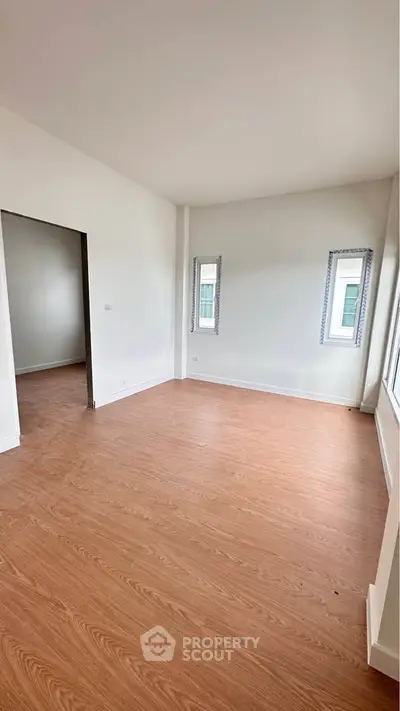 Spacious empty room with wooden flooring and large windows, perfect for customization.