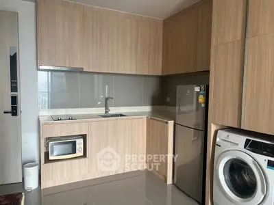 Modern kitchen with wooden cabinets, stainless steel fridge, and washing machine in sleek apartment.