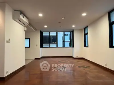 Spacious unfurnished living room with wooden flooring and large windows in modern apartment.