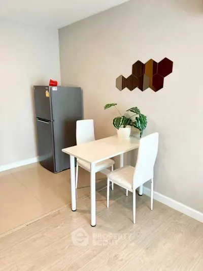 Modern dining area with sleek white table and chairs, adjacent to stainless steel fridge.