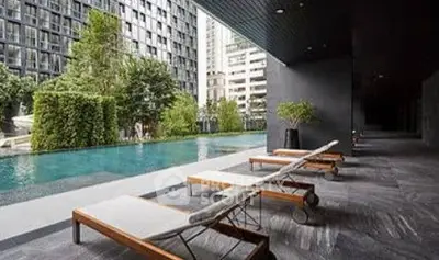 Luxurious modern apartment pool area with sleek lounge chairs and lush greenery.