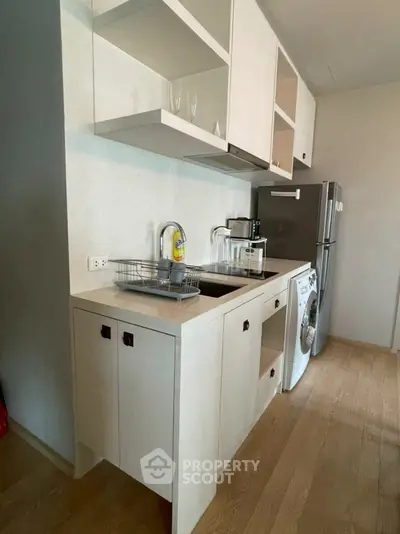 Modern kitchen with sleek cabinetry, washing machine, and stainless steel fridge in compact layout.