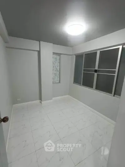 Spacious empty room with modern tiled flooring and large windows, perfect for customization.