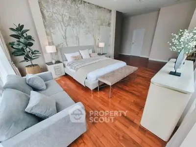 Spacious bedroom with elegant decor and hardwood floors, featuring a cozy seating area and stylish furnishings.
