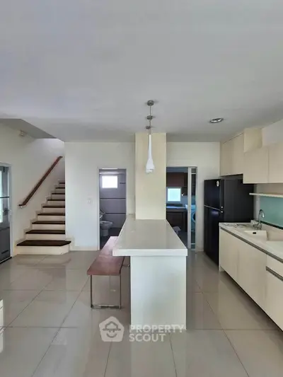 Modern kitchen with sleek cabinetry and island, adjacent to staircase and laundry area.
