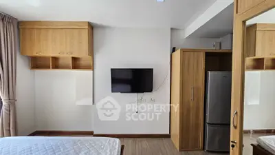 Modern bedroom with wall-mounted TV and built-in wooden storage cabinets.