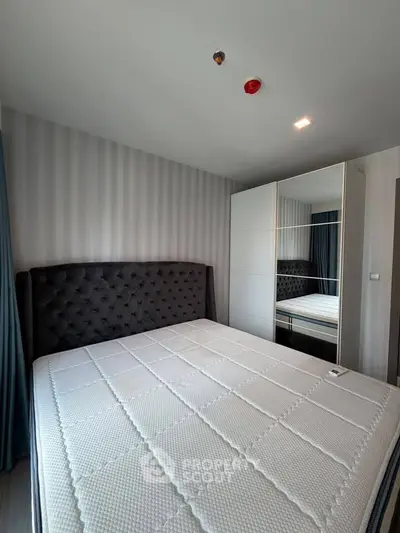 Modern bedroom with plush headboard and mirrored wardrobe in stylish apartment.
