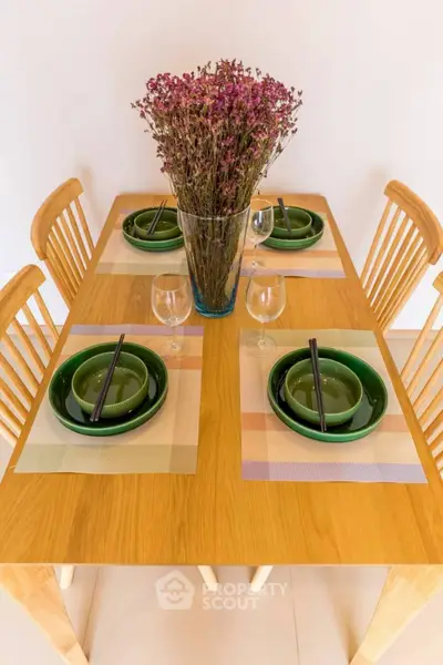 Elegant dining setup with wooden table, green dishes, and floral centerpiece.