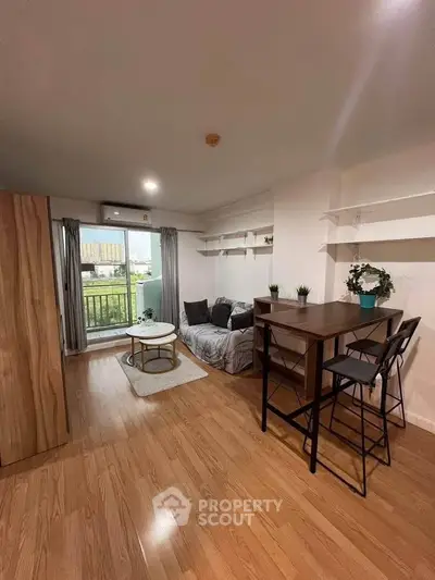 Modern living room with wooden flooring, cozy seating, and balcony access in a stylish apartment.