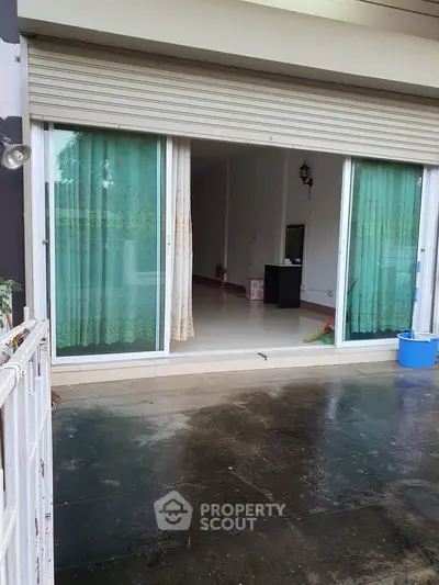 Spacious open entrance with sliding glass doors and green curtains, leading to a bright interior space.
