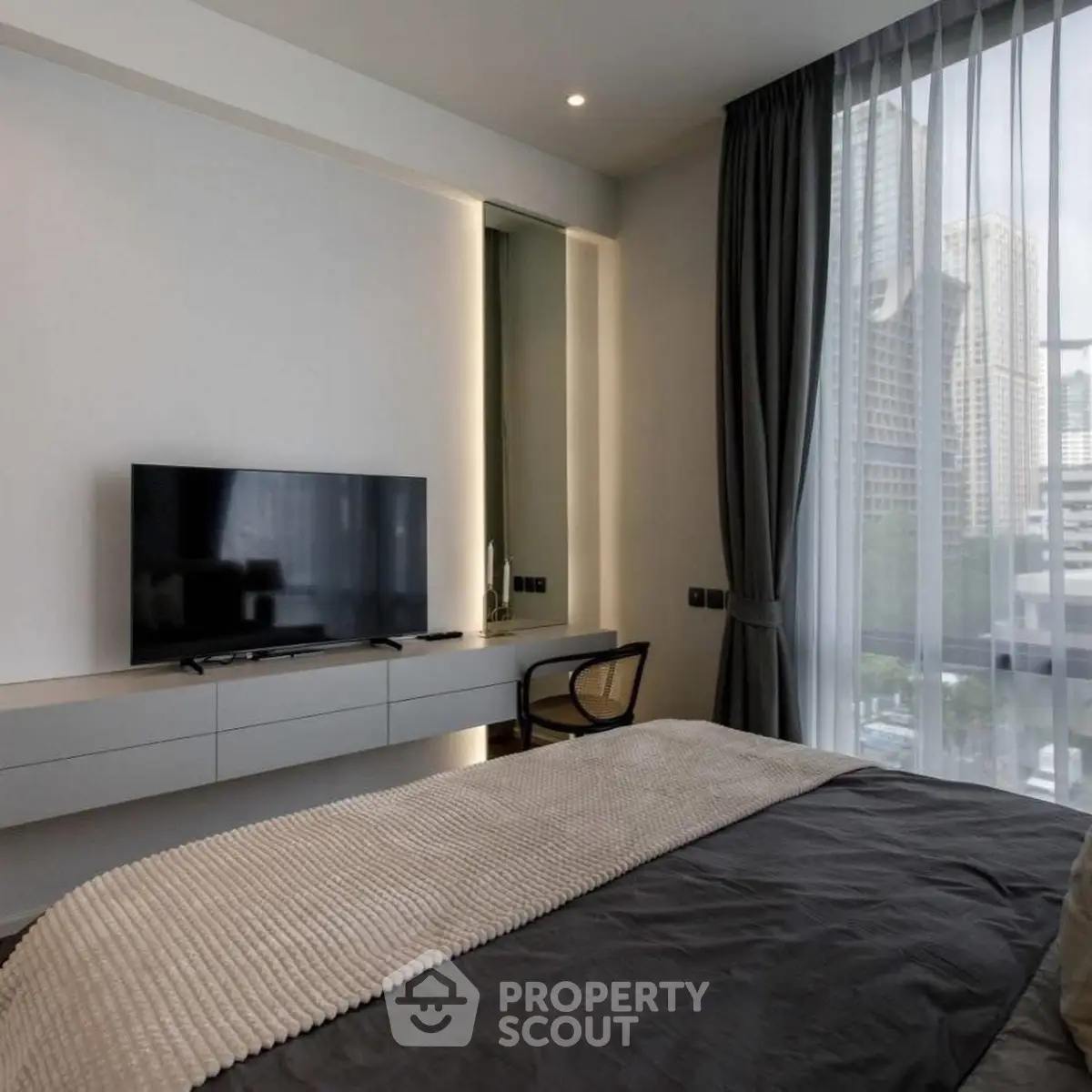 Modern bedroom with large window and city view, featuring sleek furniture and neutral tones.