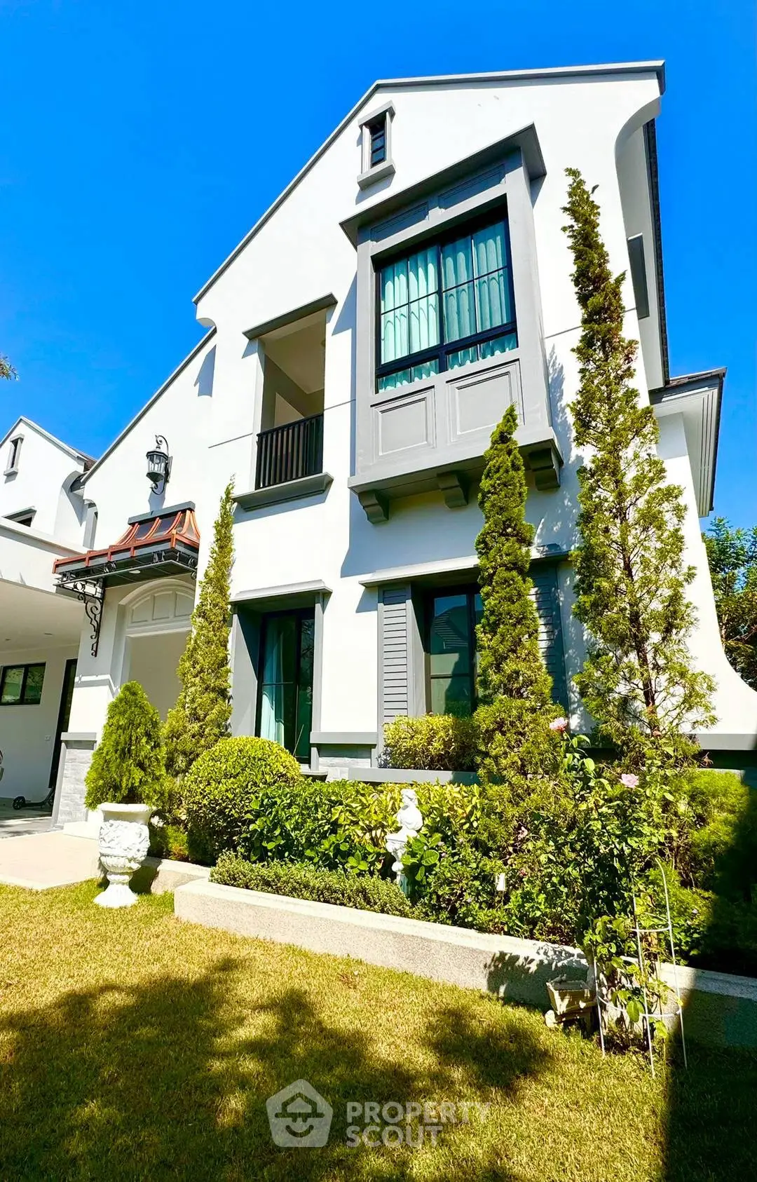 Charming two-story house with lush garden and elegant facade under clear blue sky.