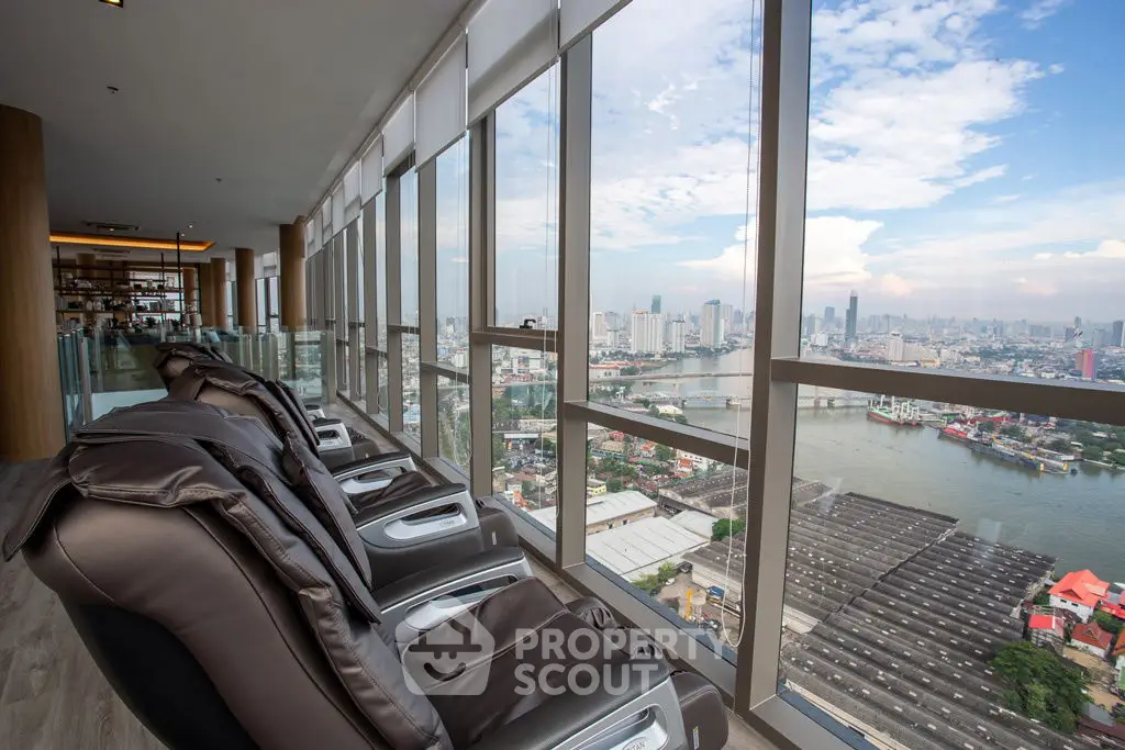 Stunning high-rise view with massage chairs overlooking cityscape and river.