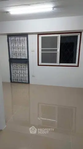 Spacious empty room with tiled flooring and barred window, ideal for customization.