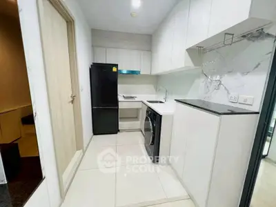 Modern kitchen with sleek white cabinets, black fridge, and integrated washing machine.