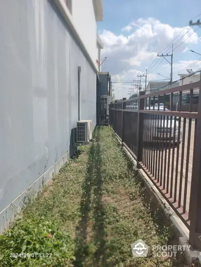 Charming narrow garden pathway alongside a modern residential building, offering a private outdoor space with potential for landscaping.