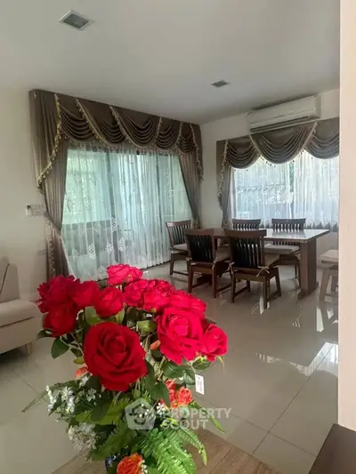 Elegant living room with large windows, luxurious drapes, and vibrant floral arrangement.
