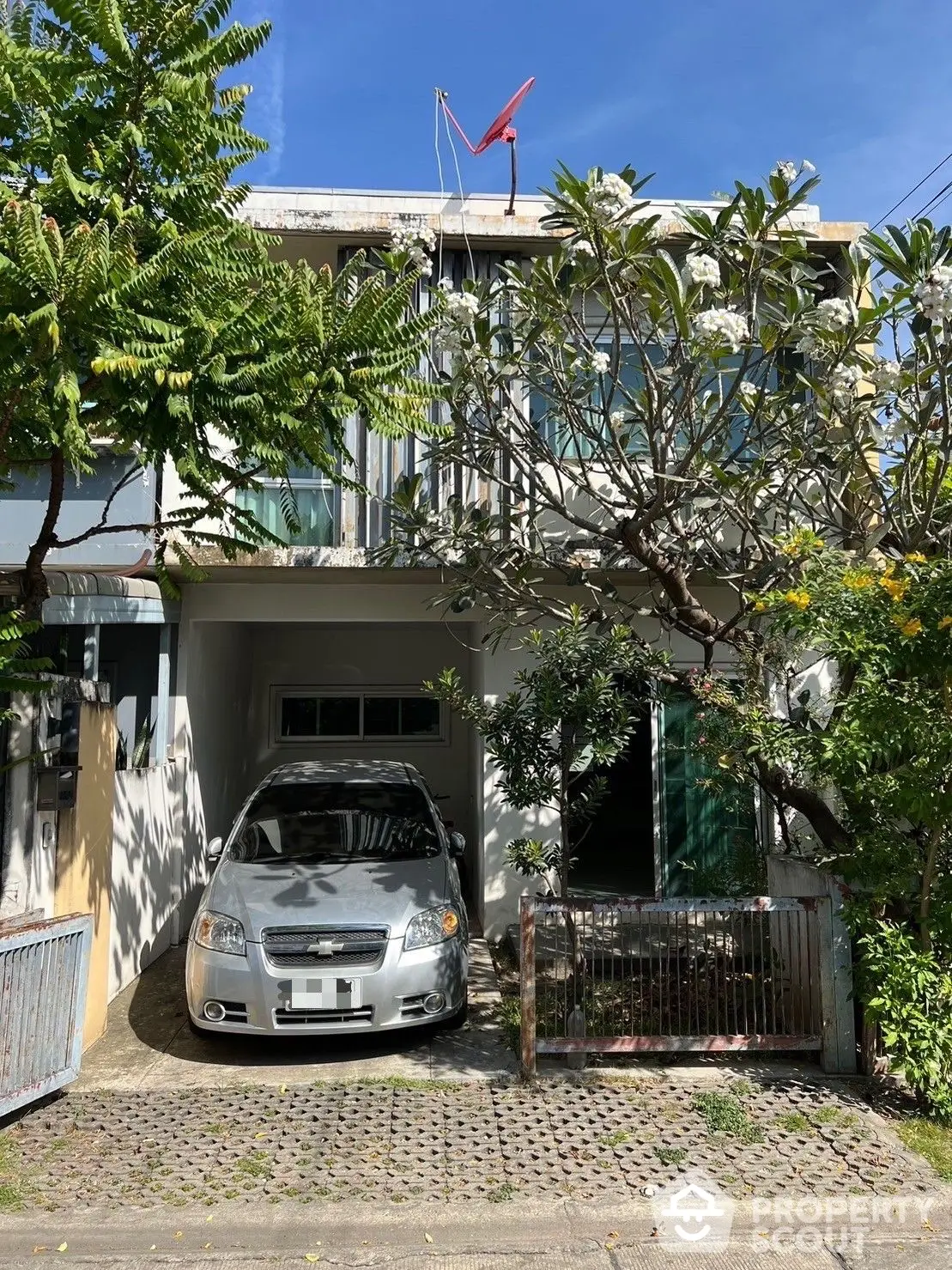 Charming two-story home with lush greenery and a spacious driveway, nestled under clear blue skies, offering a serene urban retreat.