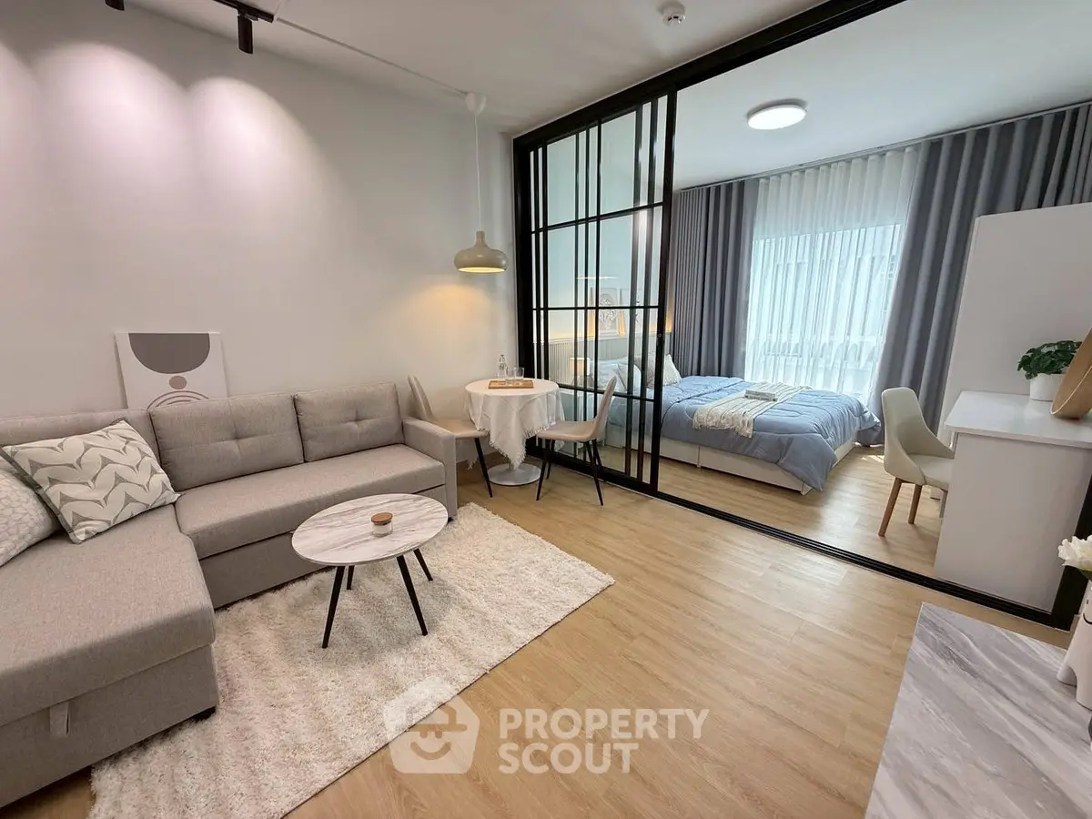 Modern open-plan living room with cozy bedroom separated by glass partition, featuring stylish decor and natural light.