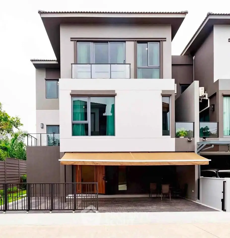 Modern multi-story house with large windows and balcony, featuring a sleek exterior design and spacious driveway.